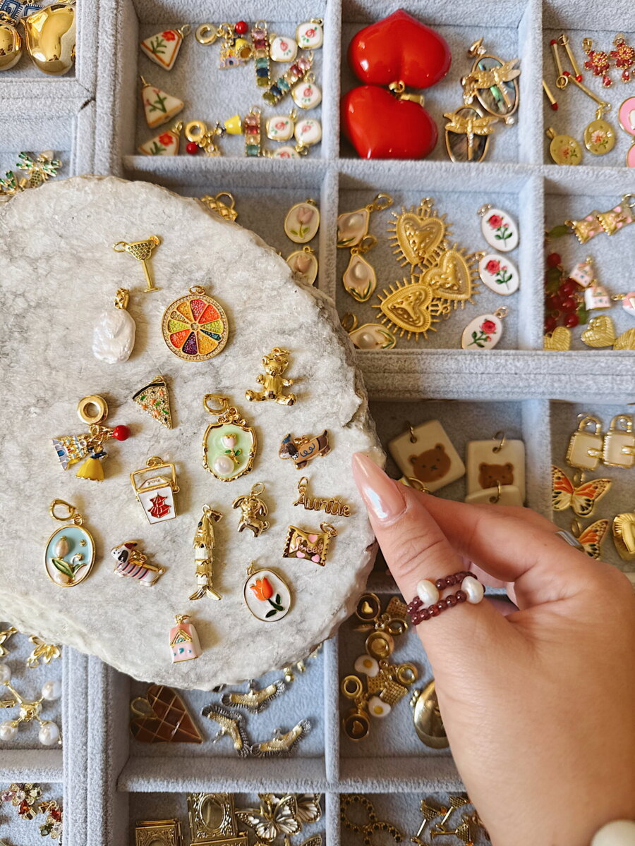 A hand holds a stone display piece covered in nostalgic accessories like a citrus slice, bear, and florals, resting over a compartmentalized tray for personalized accessories.