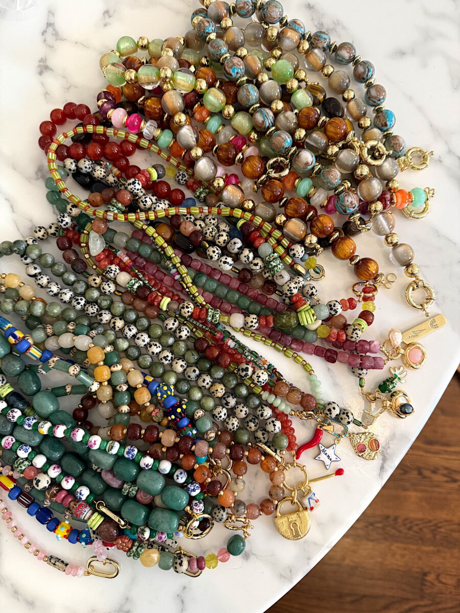 A collection of layered beaded bracelets featuring various stone, glass, and patterned beads with gold-toned clasps and charms, perfect as nostalgic accessories.