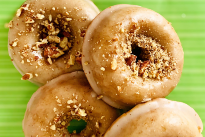 Three glazed donuts topped with crushed nuts on a green surface.