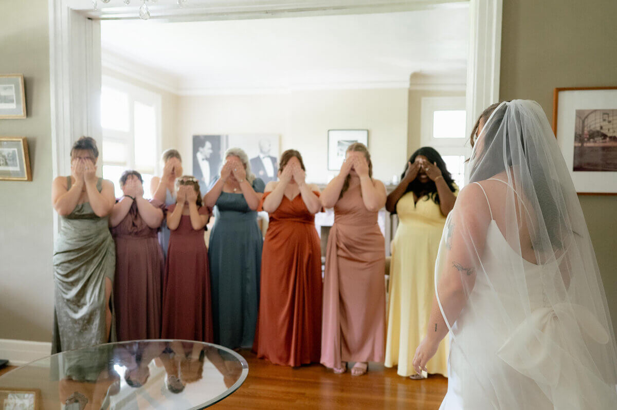 This Music-centric Memphis Wedding Even Had a Tattoo Artist! - 3 A bride stands with her back to seven bridesmaids covering their eyes in surprise during a Memphis wedding celebration.