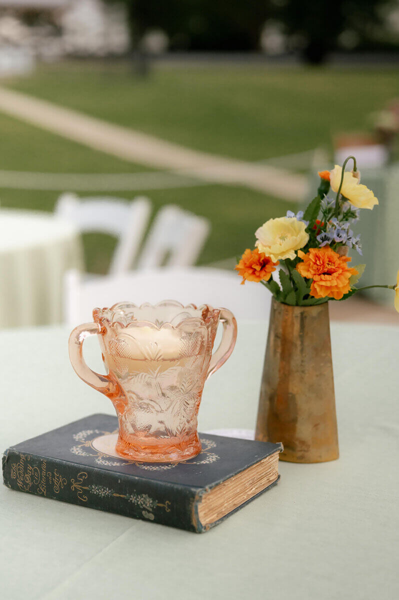 This Music-centric Memphis Wedding Even Had a Tattoo Artist! - 9 A pink glass vase sits on a vintage book next to a metallic vase filled with orange and yellow flowers on a table at a Memphis wedding.