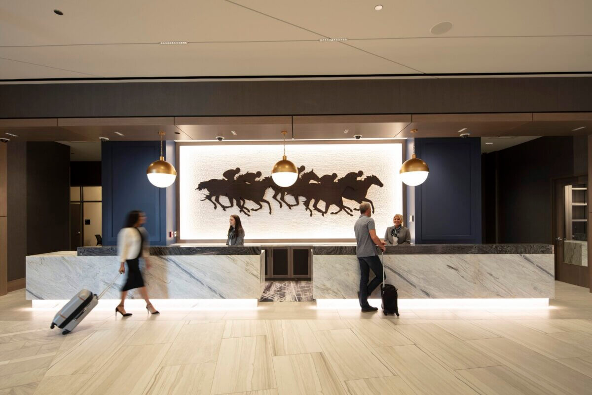 8 Lesser-Known Southern Horse Racing Venues to Know (and When to Go!) - 5 Hotel lobby reception desk with staff and a guest, positioned before a backlit wall art piece of running horses fitting for horse racing venues.