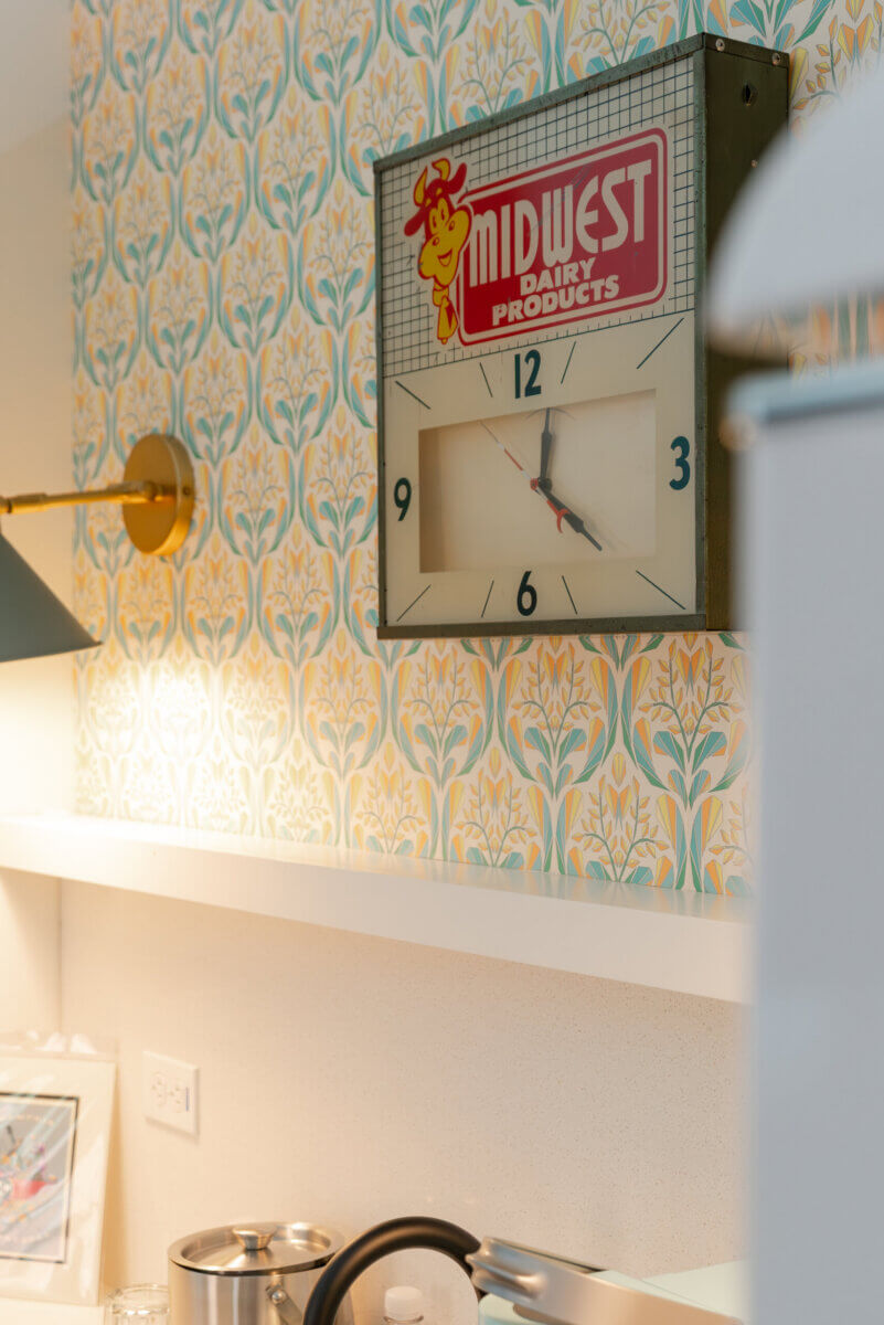 You Won't Believe What They Found Inside This 120-Year-Old Memphis Hotel - 5 A rectangular wall clock with a Midwest Dairy Products logo hangs above a shelf against patterned floral wallpaper in a historic hotel design.