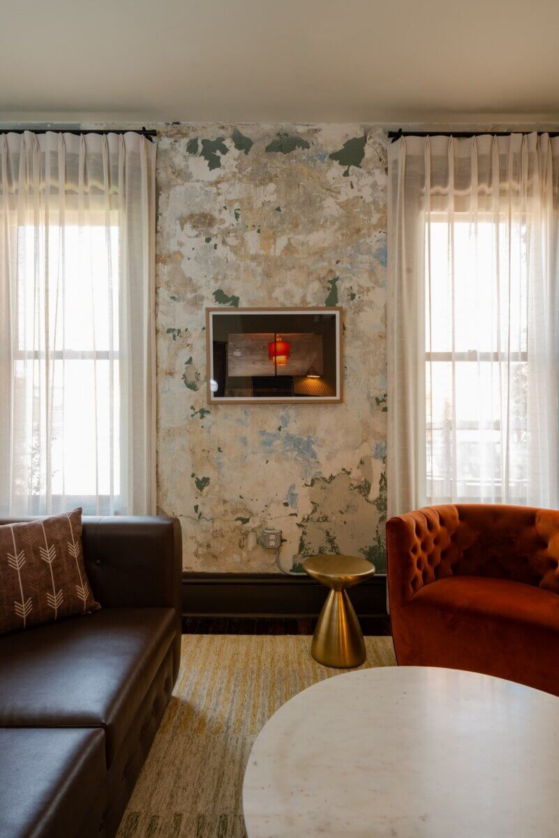 You Won't Believe What They Found Inside This 120-Year-Old Memphis Hotel - 6 A brown leather sofa and orange velvet armchair sit beside a gold side table against a wall of peeling, distressed paint in a setting of historic hotel design.