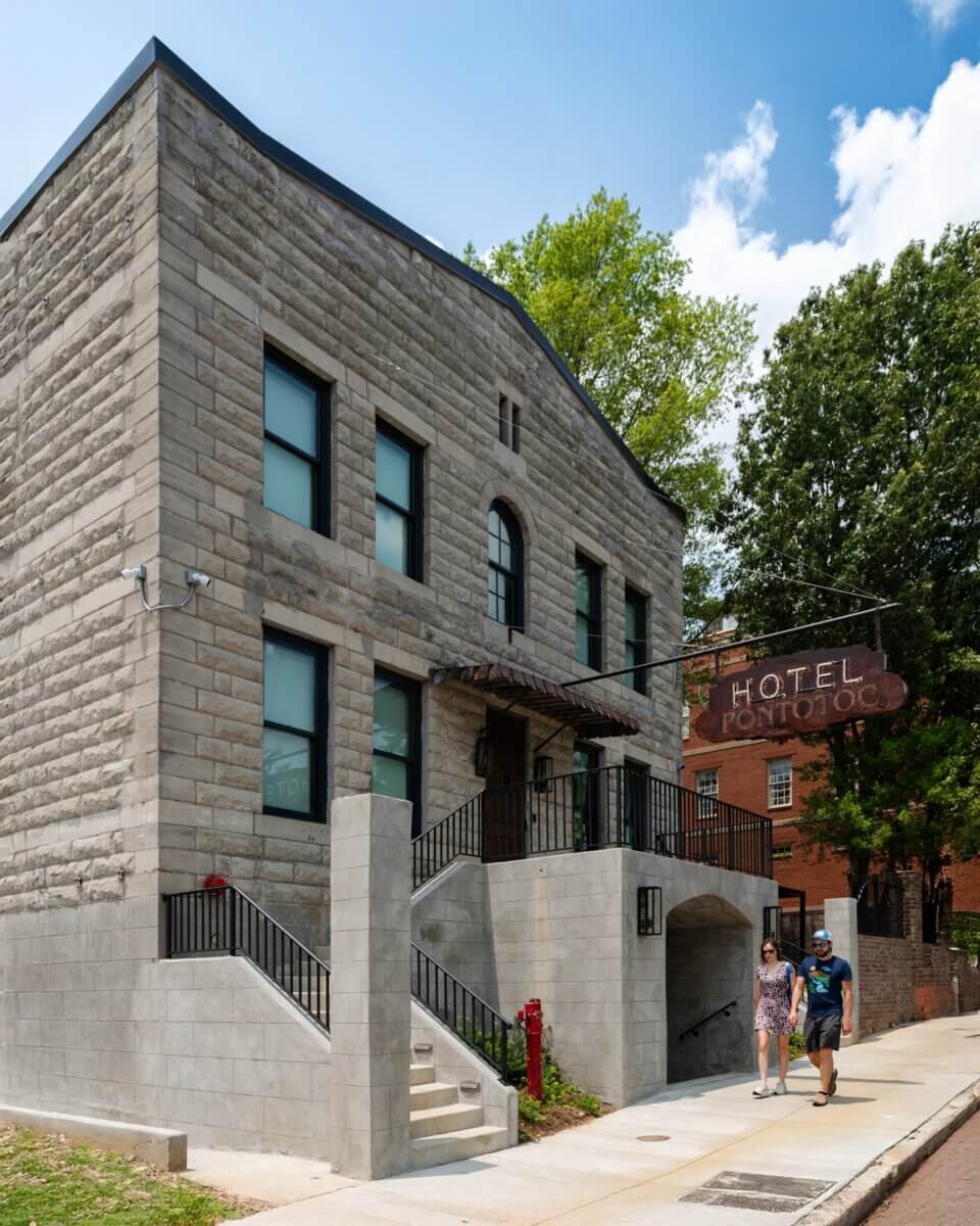 You Won't Believe What They Found Inside This 120-Year-Old Memphis Hotel - 3 Two people walk on a sidewalk in front of the stone Hotel Pontotoc building with a hanging sign.