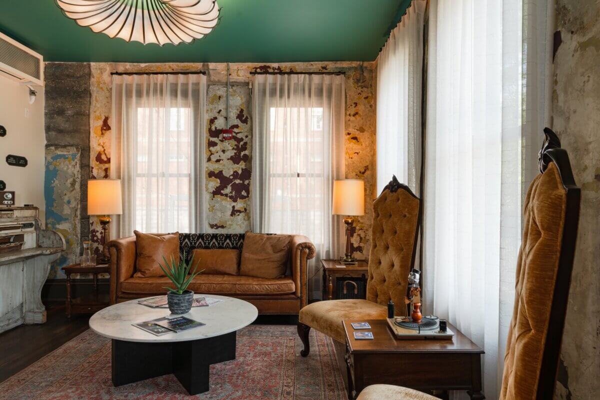 You Won't Believe What They Found Inside This 120-Year-Old Memphis Hotel - 2 A room with distressed walls, a leather sofa, a round marble coffee table, and high-backed upholstered chairs.