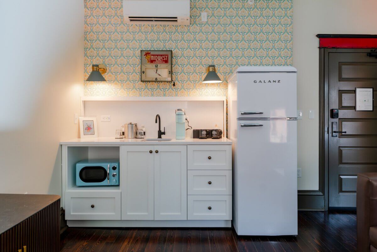 You Won't Believe What They Found Inside This 120-Year-Old Memphis Hotel - 4 A kitchenette with a white refrigerator, a blue microwave, a sink, and patterned wallpaper.