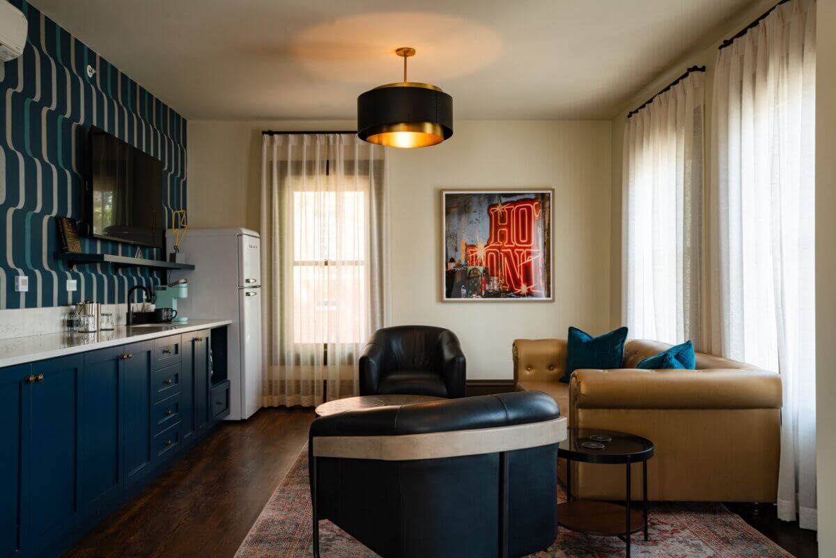 You Won't Believe What They Found Inside This 120-Year-Old Memphis Hotel - 8 A living area with a navy blue kitchenette, a tan leather sofa, and two black leather armchairs facing a neon “HOTEL” sign, capturing the boutique hotel aesthetic of Hotel Pontotoc.