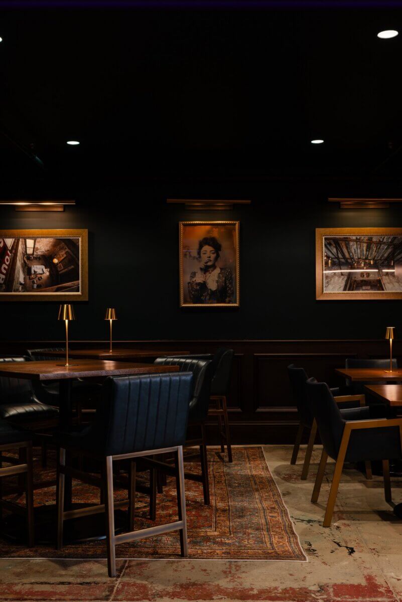 You Won't Believe What They Found Inside This 120-Year-Old Memphis Hotel - 9 Dark dining room with black walls, three framed pictures, small gold table lamps, and dark leather chairs on a patterned rug, reflecting boutique hotel design.