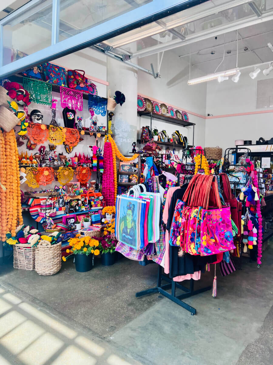 A Memphis Día de los Muertos Guide: Where to Celebrate - 5 Shop interior filled with Mexican folk art, including papel picado banners, skull figurines, marigold garlands, and colorful embroidered tote bags.