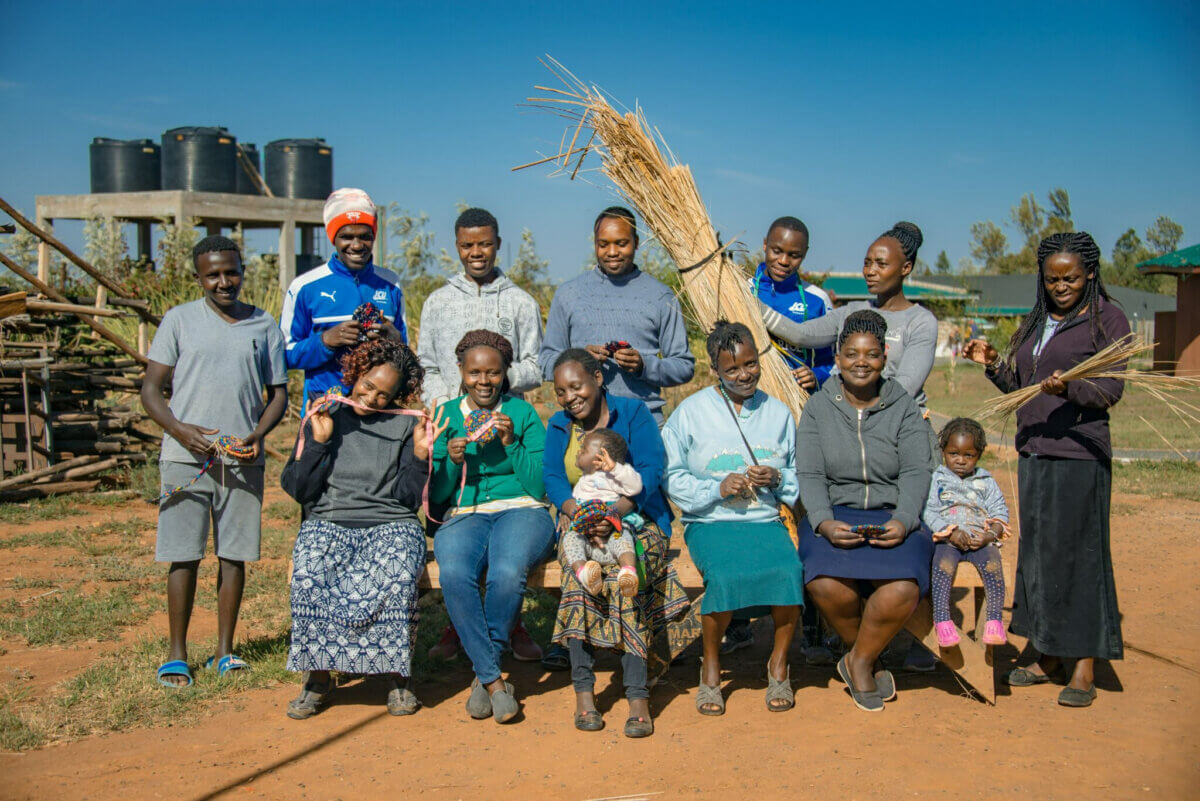 What If Your Holiday Shopping Could Change Someone's Life? - 7 A group of people sitting and standing outdoors, holding bundles of reeds and finished woven crafts.