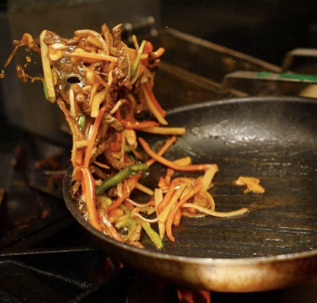 Stir-fry being tossed in a frying pan over a flame.