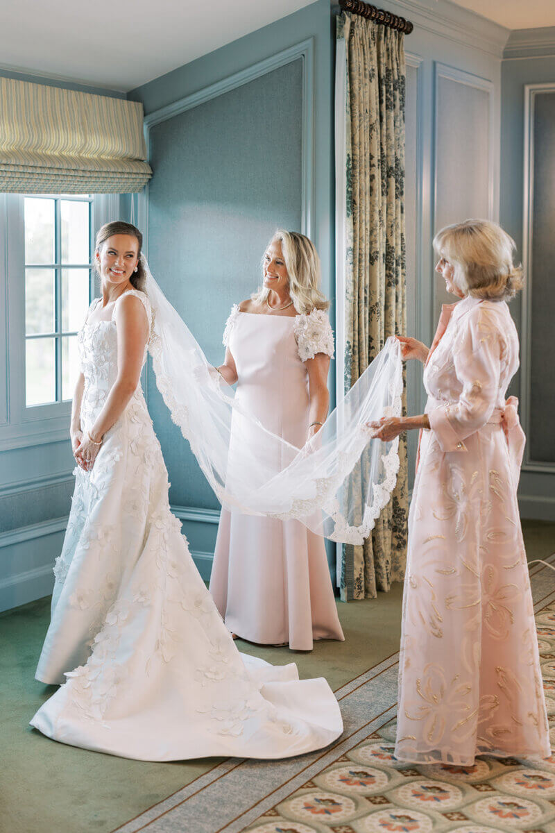 A Secret Speakeasy and Late-Night Taco Bell?! This Nashville Wedding Had Serious Surprises - 8 A bride in a floral-appliqué gown smiles at her Nashville wedding as two women in formal gowns help adjust her long lace veil.