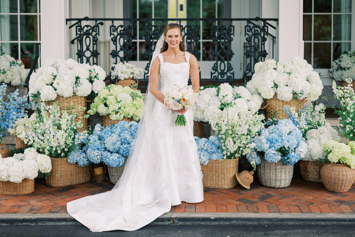 A Secret Speakeasy and Late-Night Taco Bell?! This Nashville Wedding Had Serious Surprises - 9 A bride in a white wedding gown and veil holding a bouquet, standing before a Nashville wedding display of white and blue flowers in woven baskets.