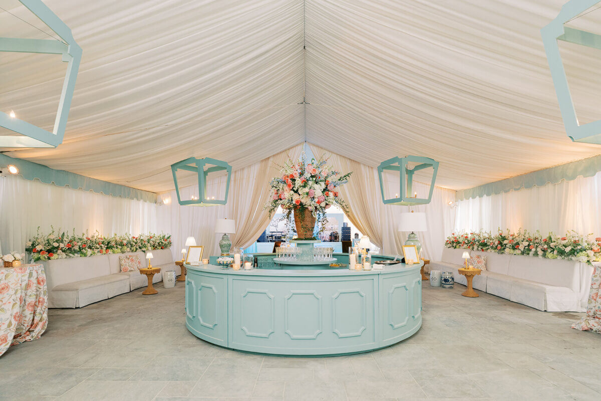 A Secret Speakeasy and Late-Night Taco Bell?! This Nashville Wedding Had Serious Surprises - 5 A light blue circular bar stands in a draped garden party wedding tent, featuring a large central floral arrangement surrounded by white sofas and hanging lanterns.