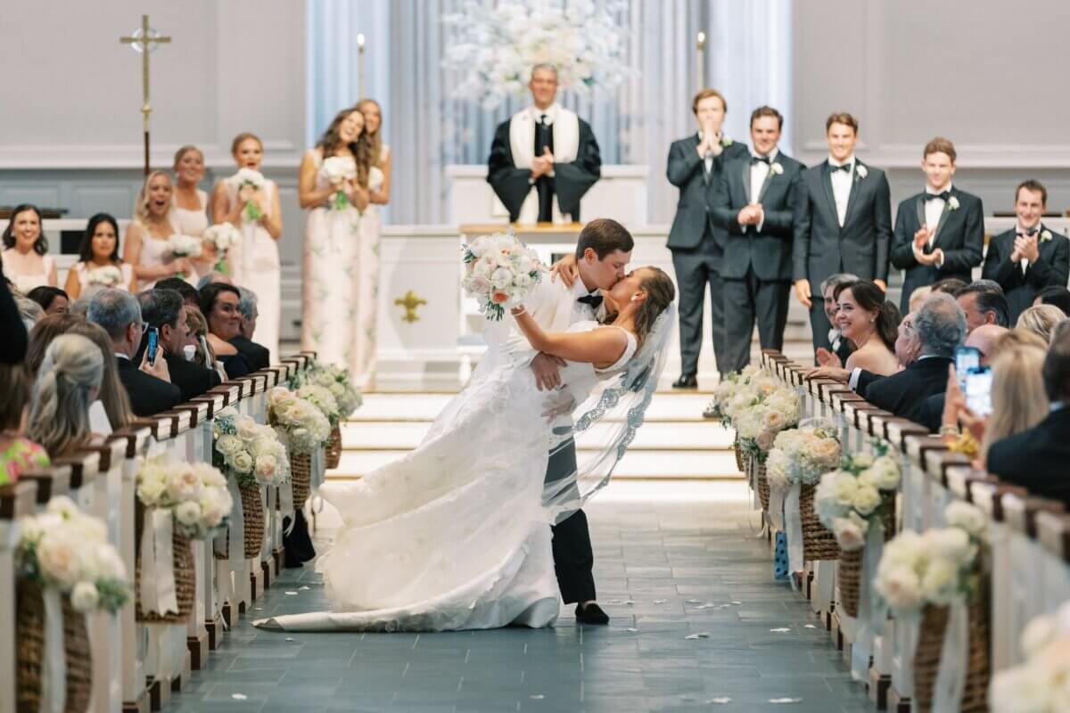A Secret Speakeasy and Late-Night Taco Bell?! This Nashville Wedding Had Serious Surprises - 12 A bride and groom share a kiss while dipping in a church aisle, offering timeless Nashville wedding inspiration as guests look on.