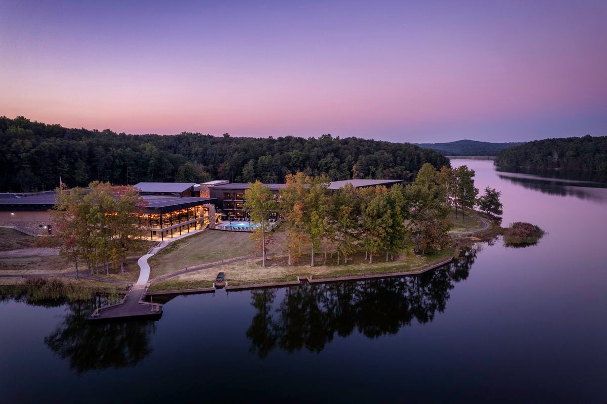 Aerial view of a resort-worthy hotel nestled in a forest along a lake at sunset, offering scenic views.