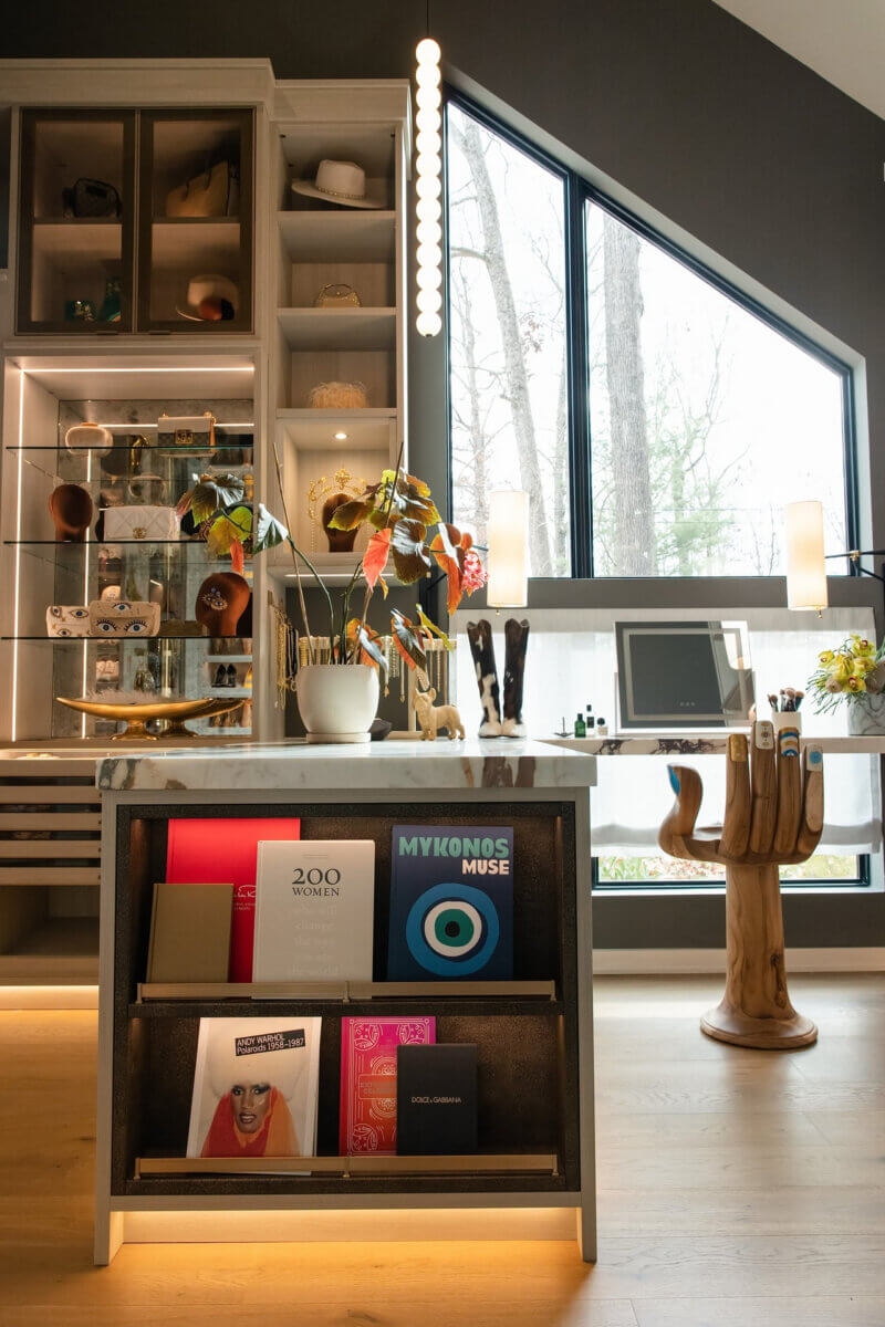 Want to Increase Your Home's Resale Value? Consider a Custom Closet - 3 A marble-topped display island featuring art books and a wooden hand-shaped stool in front of a windowed desk, a custom closet detail that adds to home resale value.