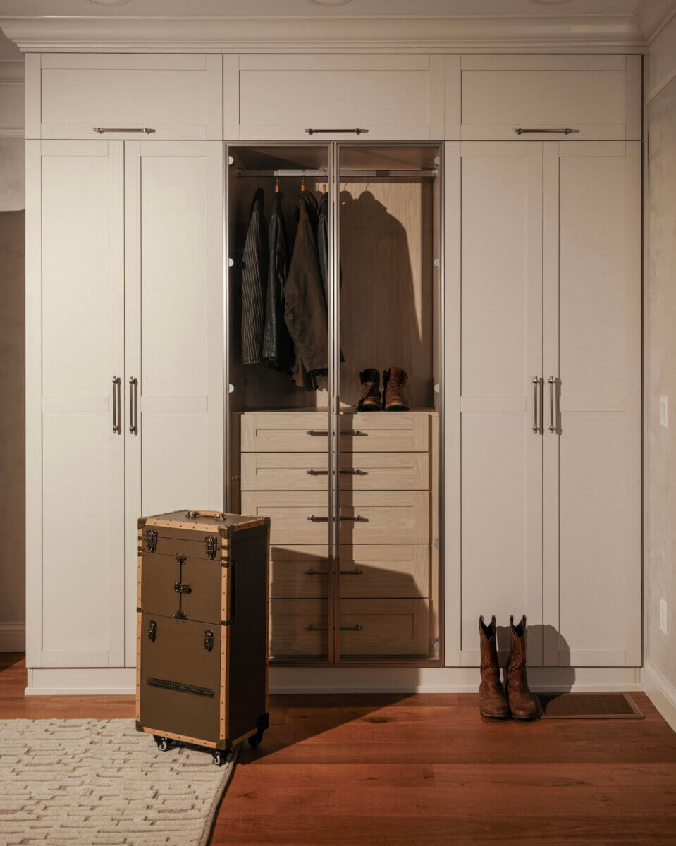 Want to Increase Your Home's Resale Value? Consider a Custom Closet - 6 A beige custom closet with open doors reveals hanging clothes, drawers, and boots. A vintage suitcase stands in front, adding charm and home resale value.