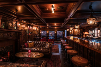 A dark, wood-paneled Nashville private club bar featuring a leather sofa, a coffee table, and a long wooden bar with a row of round stools.