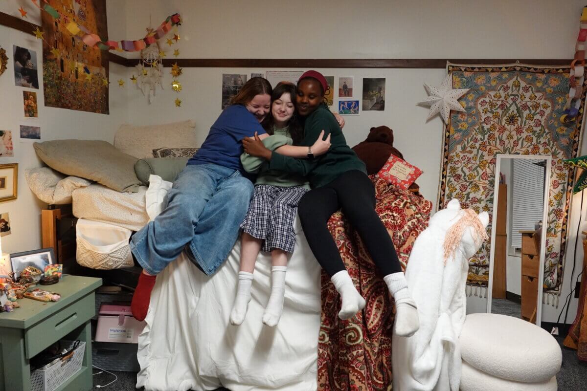5 Reasons This Idyllic TN Private School Might Be Right for Your Family - 7 Three college prep high school friends hug while sitting on a bed in a decorated dormitory room.