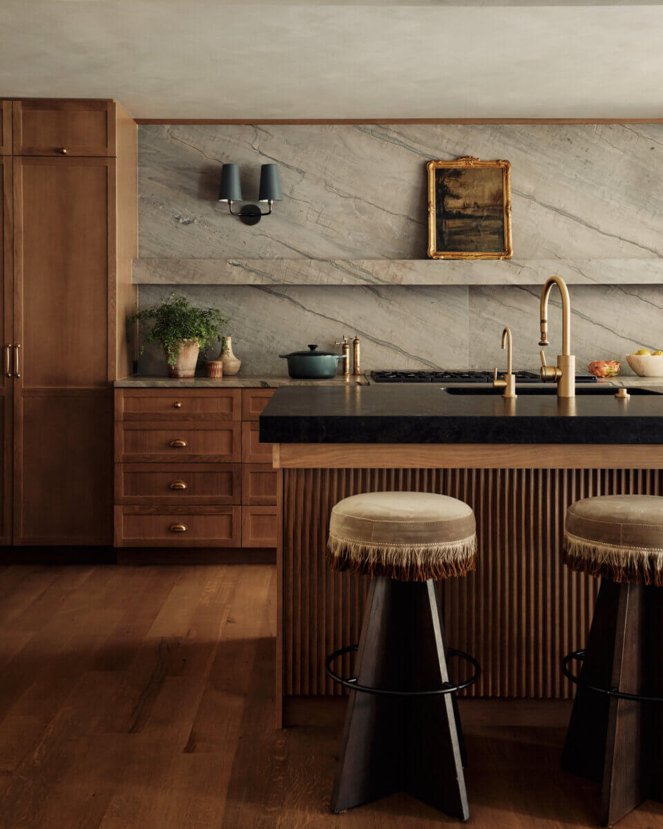 They Abandoned Their Dream Home Plans. Here's What Happened Next. - 9 A kitchen with wooden cabinets, a stone backsplash, a black countertop island with two stools, and a small framed painting on the wall.