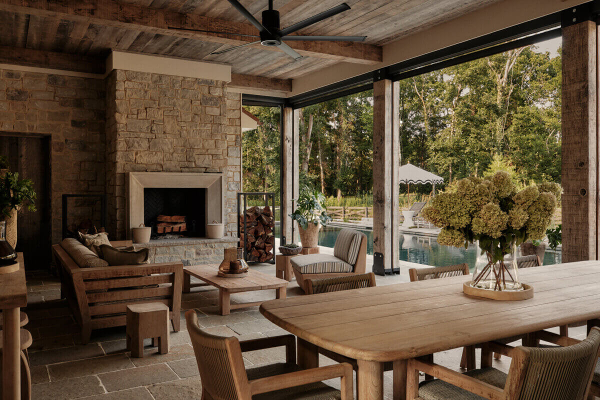 They Abandoned Their Dream Home Plans. Here's What Happened Next. - 10 A covered stone patio with a fireplace, lounge seating, and a dining table overlooking a swimming pool and trees.