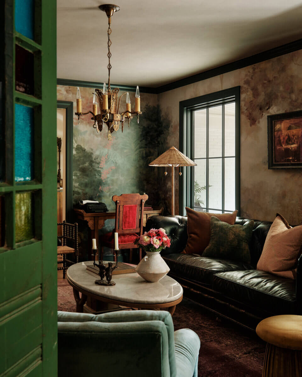 They Abandoned Their Dream Home Plans. Here's What Happened Next. - 13 A dimly lit living room with dark walls, a leather sofa, a marble coffee table with a flower vase, and a vintage chandelier.
