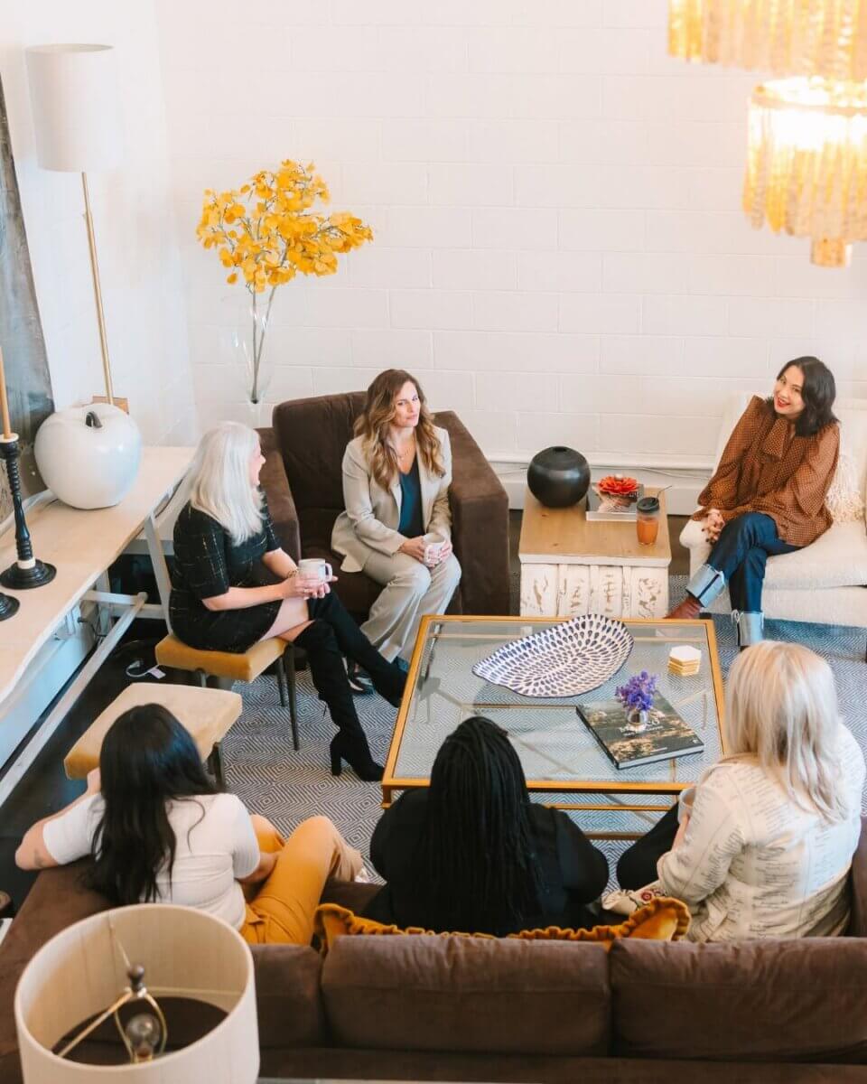 Five women sitting in a living room during a BrainTrust meeting for business expansion.