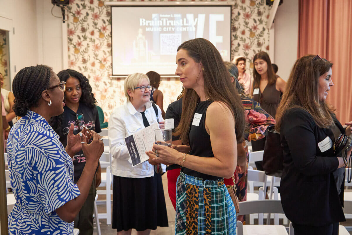 A diverse group of women gathered for a BrainTrust event, socializing and holding remote business materials.