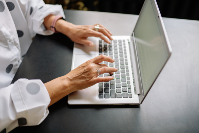Hands typing on a silver laptop on a black desk, driving business expansion.