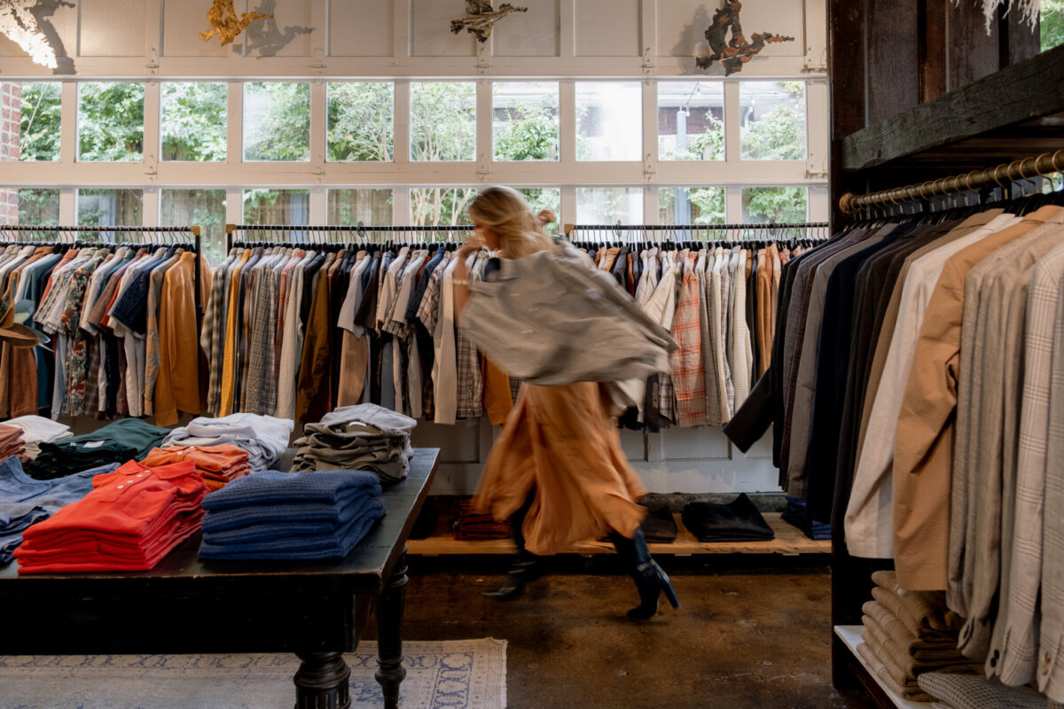 Closet Organization Tips for Revamping Your Wardrobe (Without Starting From Scratch) - 2 A person in a skirt and jacket walks quickly through a clothing store with racks of shirts and coats, embodying the practice of mindful consumption.