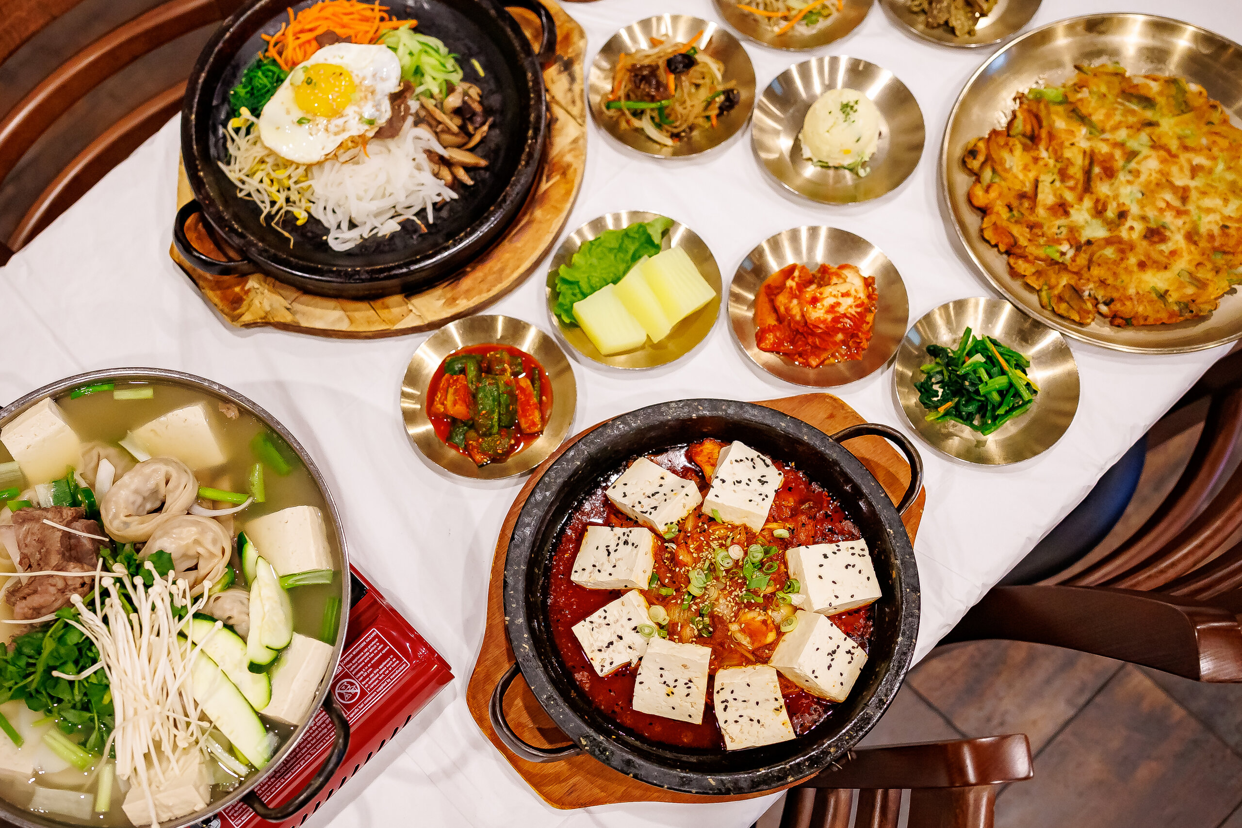 The Best Culinary Hot Spots in the South - 10 A Korean meal featuring hot pots of tofu and mixed vegetables with egg, a savory pancake, and side dishes like kimchi and greens, found at some of the best southern restaurants.