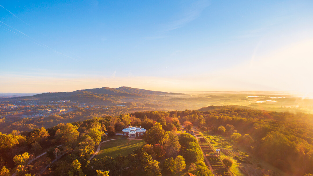 Aerial view of Monticello surrounded by autumn trees at sunrise, a picturesque highlight for Virginia weekend getaways, with a hazy mountain landscape in the distance.