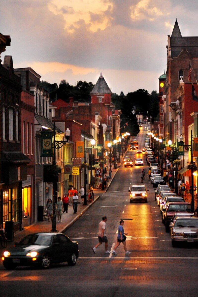 Cars and pedestrians on a street lined with historic brick buildings at sunset, an ideal scene for Virginia weekend getaways.