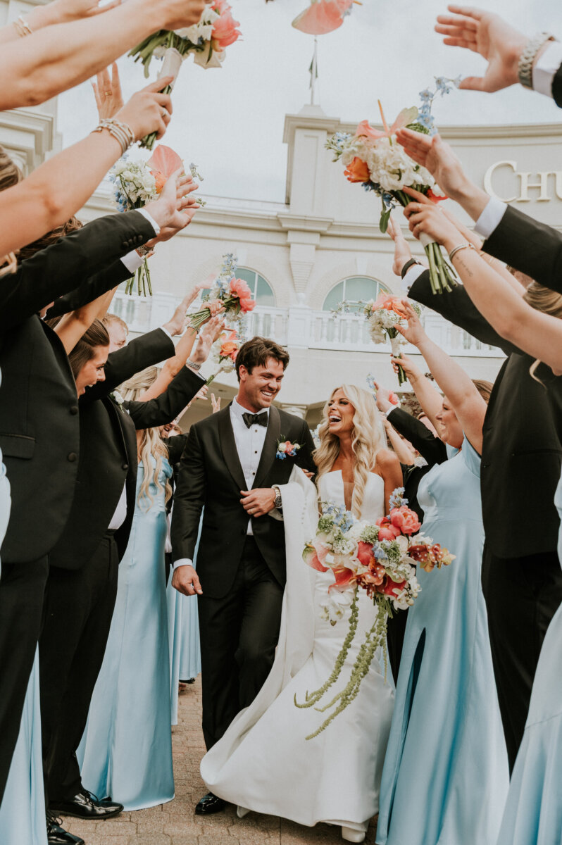 A bride and groom walk together through a tunnel of raised flower bouquets held by their wedding party at the Kentucky Derby Museum.