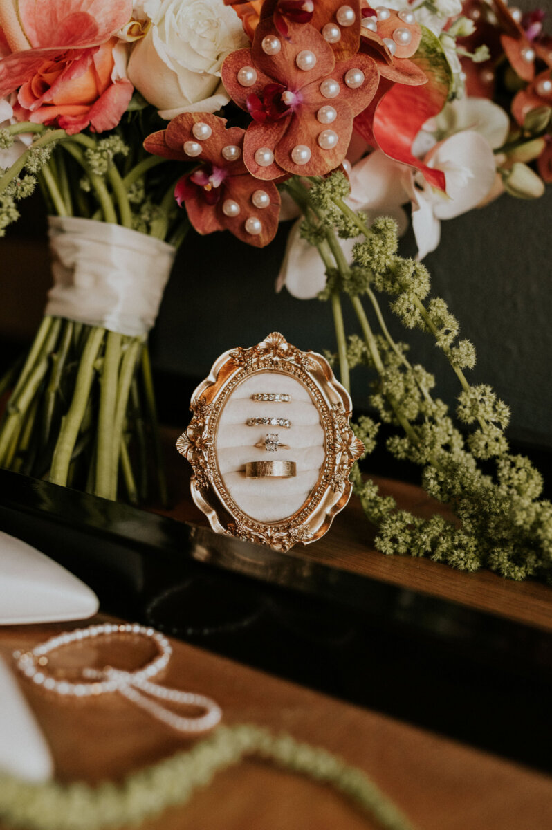 Four wedding rings displayed in an ornate gold frame at the Kentucky Derby Museum, set before a colorful flower bouquet.