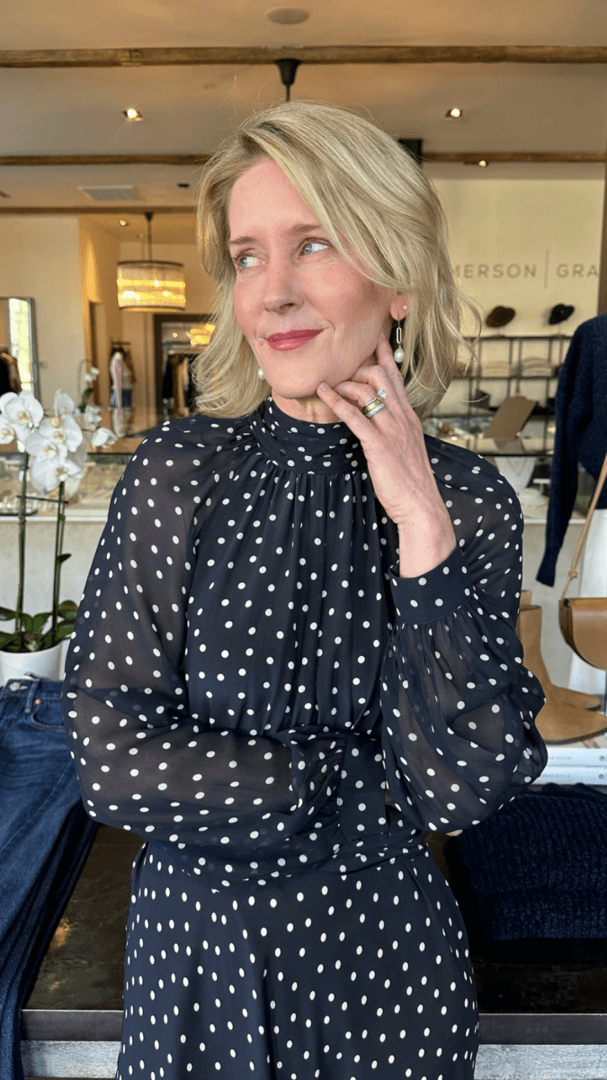 Darci Bolenbaugh poses with her hand to her chin, wearing a black long-sleeved dress with white polka dots.
