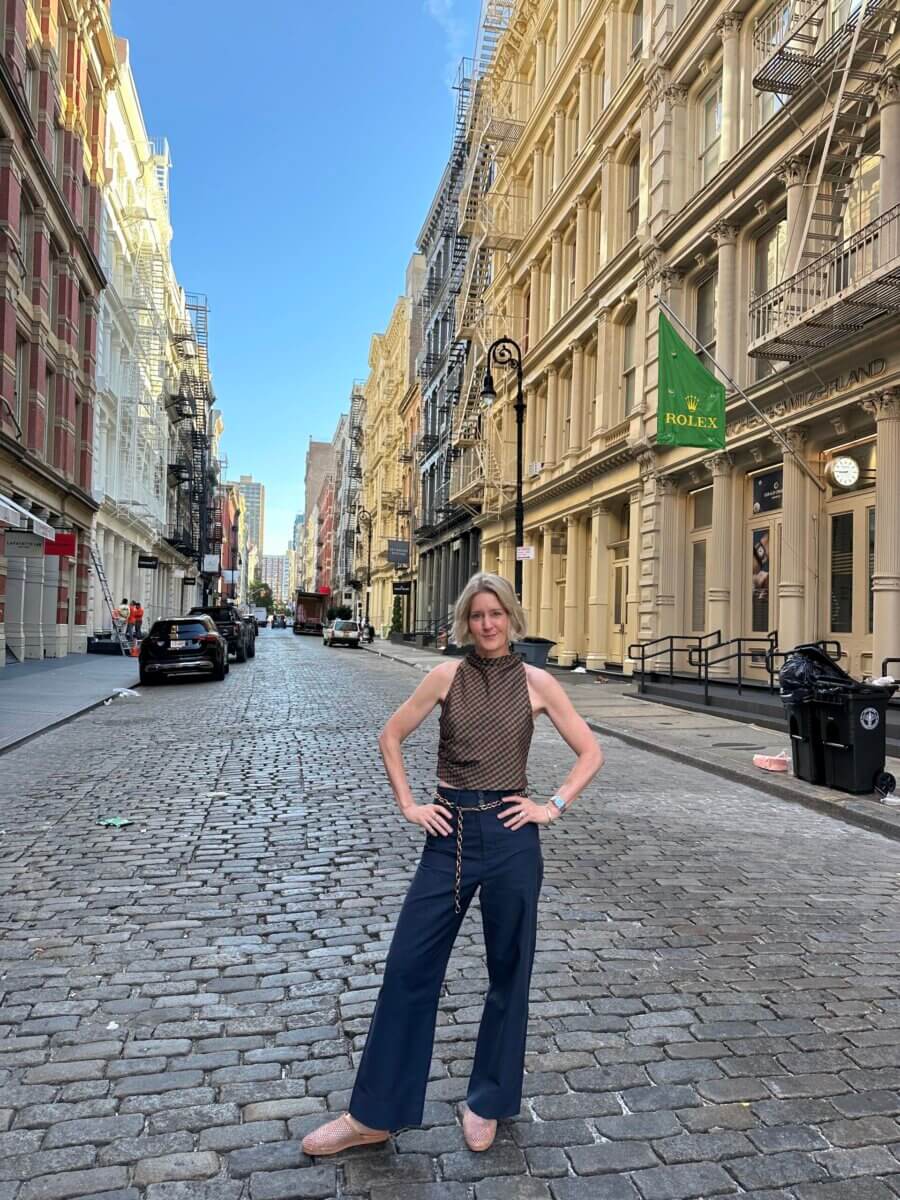 Darci Bolenbaugh stands with hands on her hips in the middle of a cobblestone street lined with historic multi-story buildings.