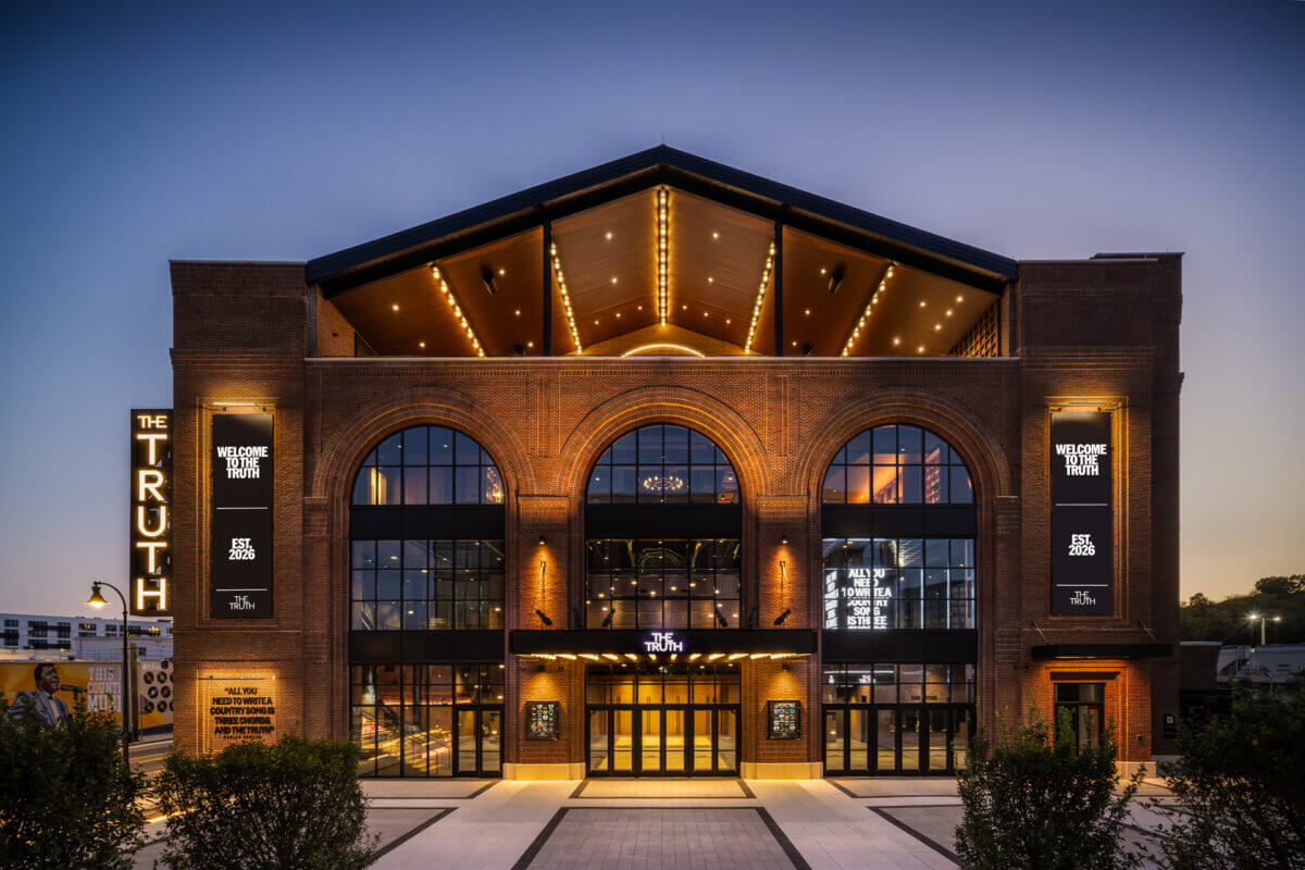 Exterior of Sally Williams’ The Truth brick building at dusk, with large arched windows and vertical banners reading “Welcome to The Truth Est. 2026.”