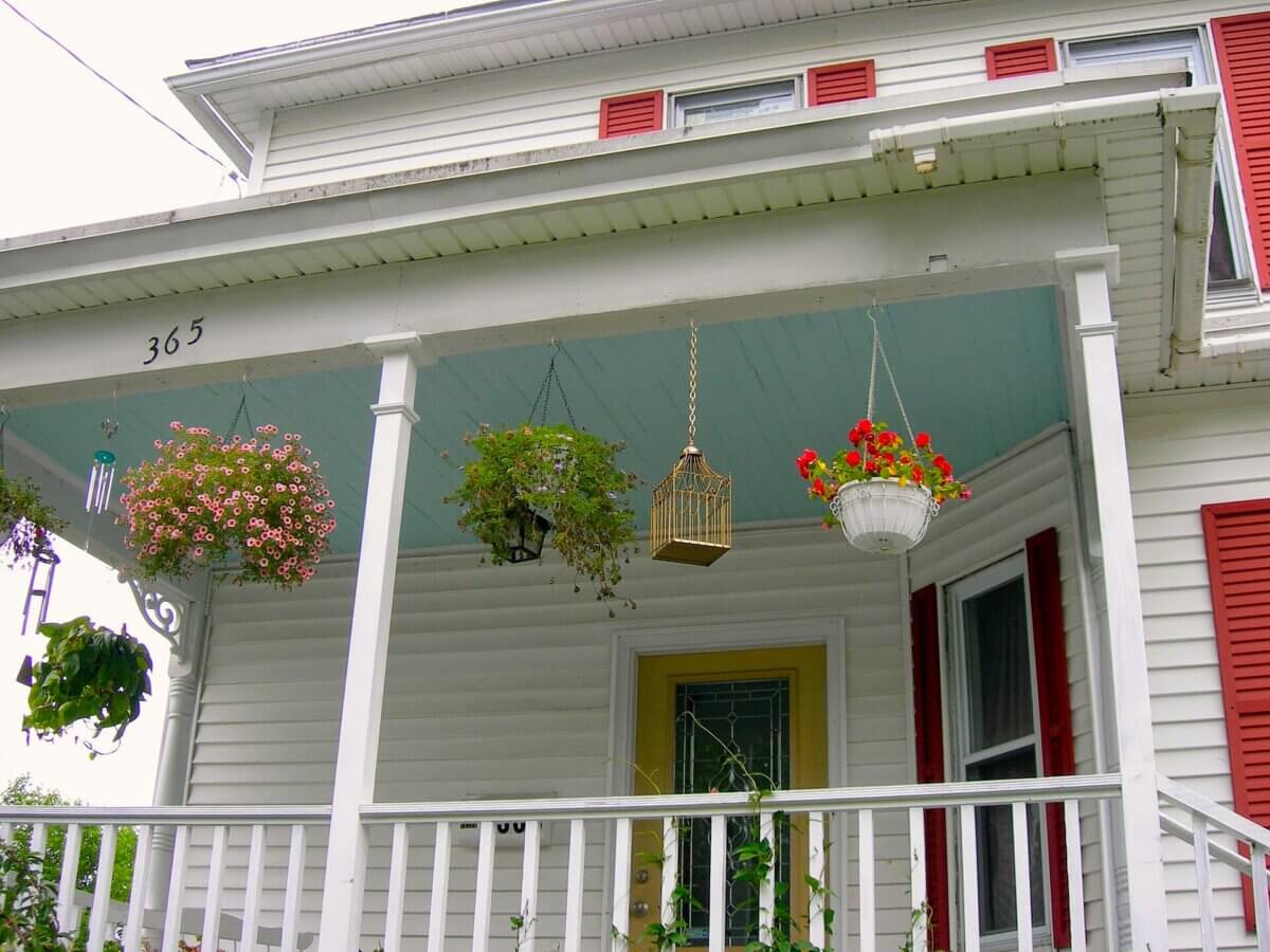 7 Spooky Southern Legends That'll Make You Lock Your Door Tonight - 2 Front porch of a white house with address number 365, featuring hanging flower baskets and a birdcage decoration that evokes a sense of Southern gothic folklore.