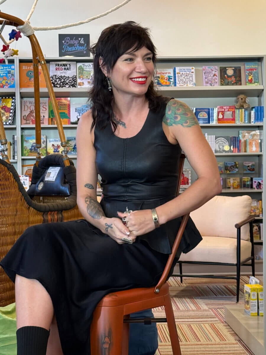 The Haunted Folklore of Mississippi Influenced This Costume Designer's Career - 3 A costume designer with a dark mullet and red lipstick sits in a chair in front of a bookshelf filled with children’s books.