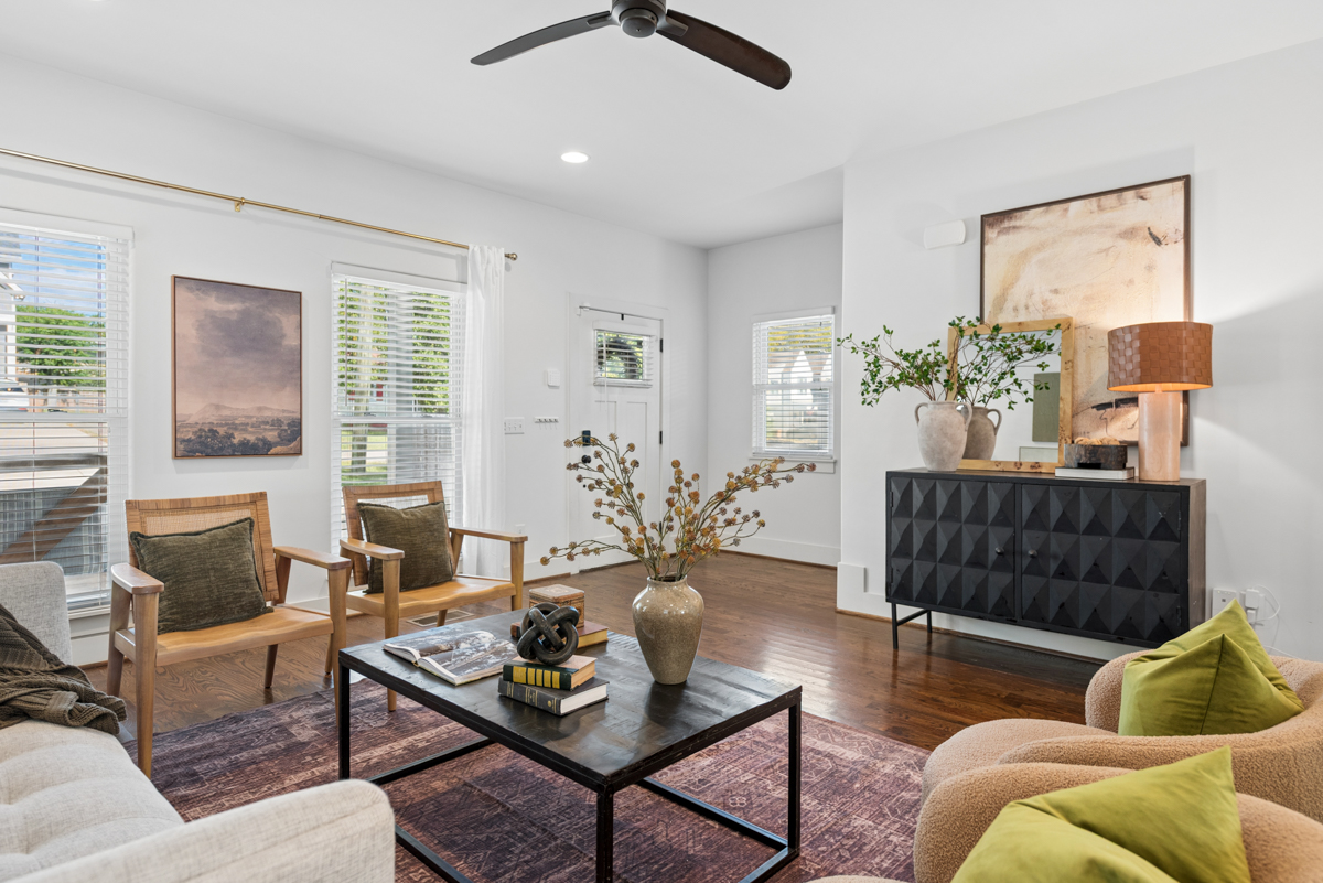 Living room at 6363 Columbia Ave featuring two wooden chairs, a black coffee table with books, and a black sideboard with a lamp and mirror.