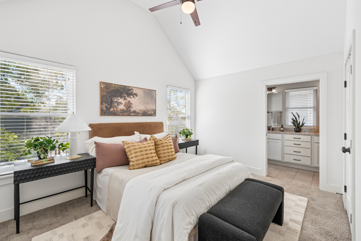 Bedroom at 6363 Columbia Ave featuring a queen-sized bed, dark metal nightstands with lamps, a charcoal bench at the foot of the bed, and an open doorway leading to a bathroom.