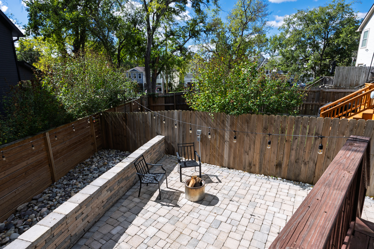 A paved backyard patio at this 6363 Columbia Ave Nashville home features two metal chairs, a cylindrical fire pit filled with logs, and string lights hanging above a wooden fence.