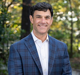 A man in a white collared shirt and a blue plaid blazer smiles outdoors at 1857 Overton Park Avenue in Memphis, Tennessee.