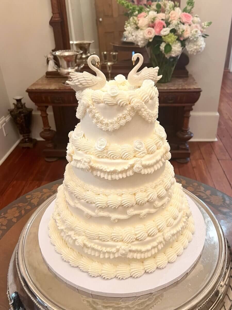 Tall white wedding cake with piped buttercream shells, white sugar roses and two swan toppers